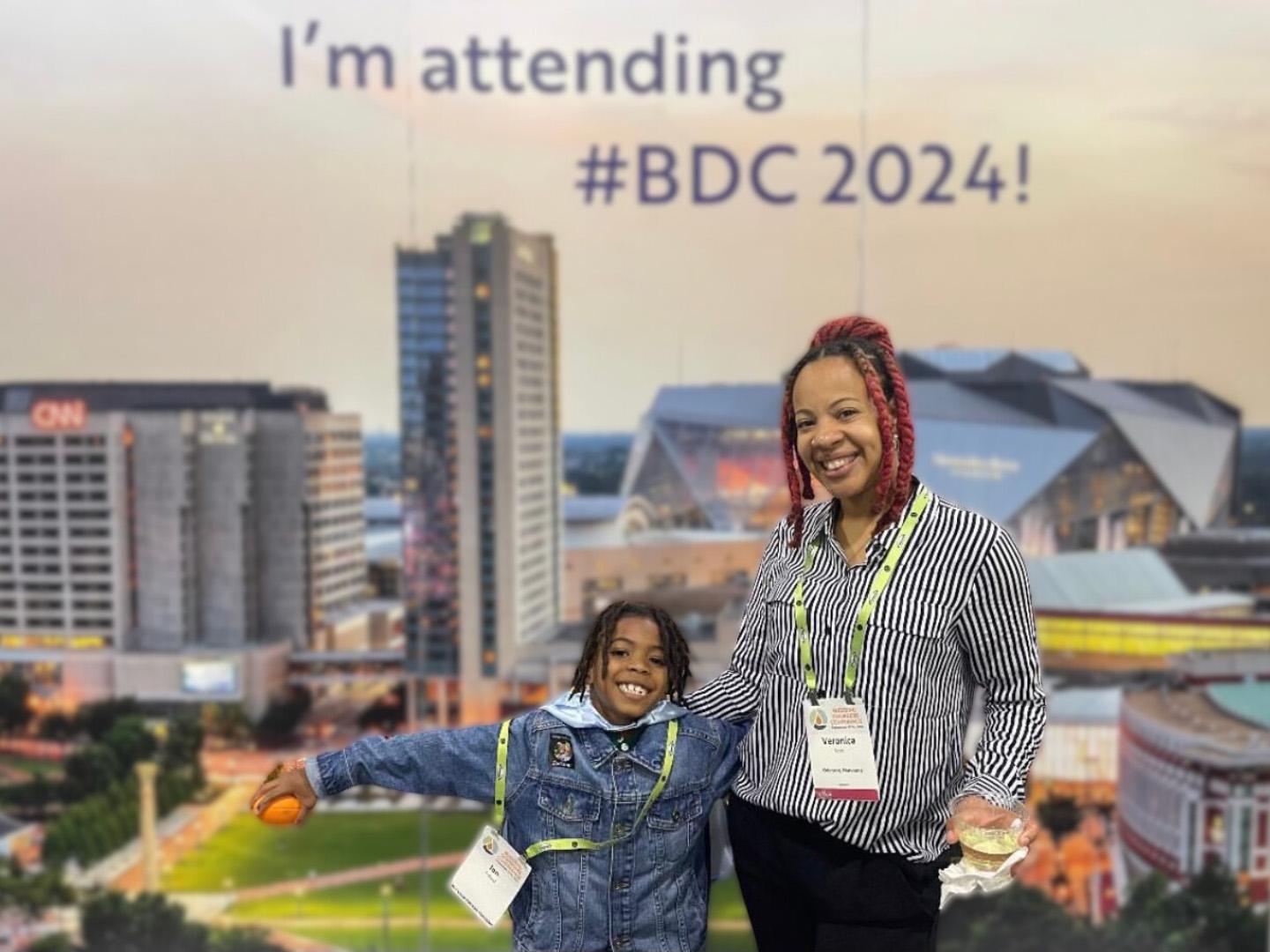 Mother and son at BDC in 2024 with a sign that reads "I'm attending #BDC2024!"